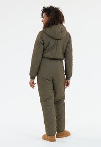 Olivi vihreä tikattu haalari, jossa on huppu, varustettuna ribbaolla varustetuilla hihansuilla ja tiukalla muotoilulla. Pehmeä pinta, jossa on timanttineliökuvio.