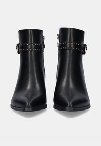 Botas negras hasta el tobillo, hechas de cuero suave, con punta afilada, acentuadas por una correa con tachuelas y herrajes metálicos. Cierre con cremallera lateral.