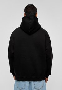 Zwarte hoodie met een ruime snit, voorzien van een grote, zachte capuchon en geribbelde manchetten. Het kledingstuk is gemaakt van een gladde, sweatshirt-achtige stof.