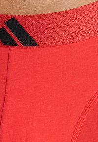 Röda sportunderkläder med en texturerad midjeband i svart med tre ränder. Slät tyg och tight passform för komfort och stöd.