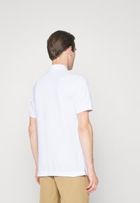 Weißes Poloshirt mit kurzen Ärmeln und klassischem Kragen, aus glattem Stoff gefertigt, mit seitlichen Schlitzen und einer sauberen, taillierten Passform.