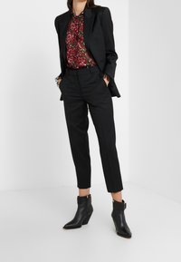 Traje negro a medida con blazer ajustado, blusa de gasa con estampado floral y pantalones negros recortados. Botines negros de tacón completan el look.
