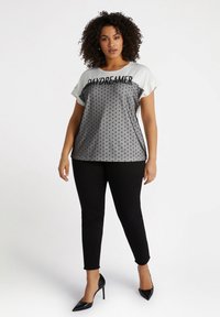 Top corto de manga corta en gris y blanco con el texto "DAYDREAMER", patrón de lunares, combinado con pantalones skinny negros y tacones altos negros.