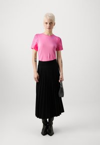 Pink short-sleeve top with eyelet detail, paired with a black pleated skirt and black knee-high boots, holding a small black handbag.