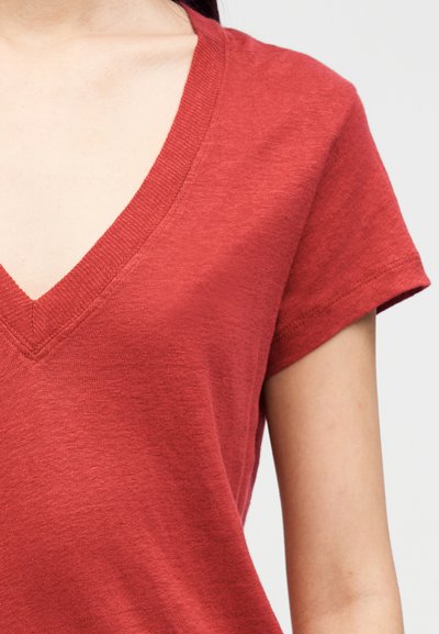 T-shirt vermelha de manga curta com design de decote em V, apresentando uma textura suave e acabamento ligeiramente mesclado. Sem padrões ou detalhes visíveis.