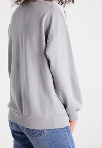 Gray sweatshirt with a relaxed fit, ribbed cuffs and hem, soft texture, and dropped shoulders, paired with light blue jeans.