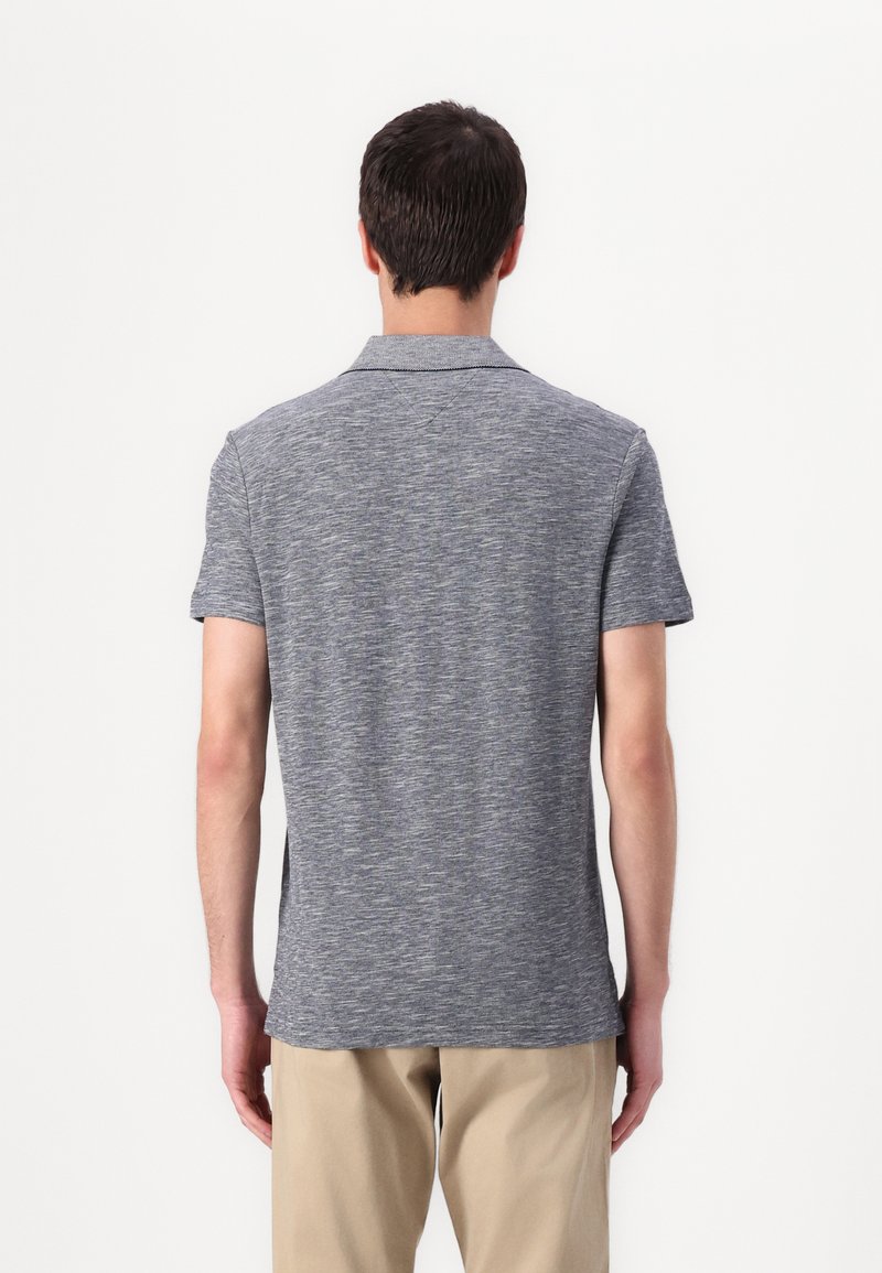 Camisa polo gris de manga corta con una tela texturizada, que presenta un cuello clásico y un dobladillo recto, combinada con pantalones en tono beige claro.