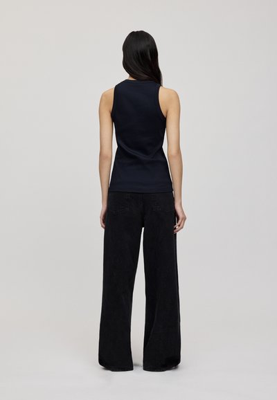 Navy sleeveless top paired with wide black jeans. The top features a fitted design, smooth texture, and minimal stitching details.