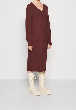 Person wearing a long-sleeve, V-neck, ribbed burgundy midi dress with tall, lace-up off-white boots on a plain background.