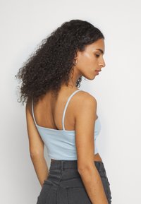 Top cropped azul claro com alças finas, textura suave e corte reto nas costas, combinado com jeans de cintura alta cinza escuro.