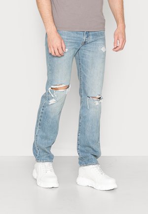 Jeans de tiro alto de color azul claro con detalles desgastados y corte recto, combinados con zapatillas blancas gruesas.