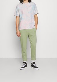 Marmorerad pastell t-shirt i blått och rosa, kombinerad med gröna sweatpants som har en sid söm och logotyp. Skor: svarta och vita sneakers.