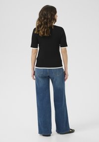 Černý pletený top s krátkými rukávy a bílým lemem, kombinovaný s volnými modrými denimo kalhotami. Zadní pohled ukazuje jednoduché linie a ležérní střih.