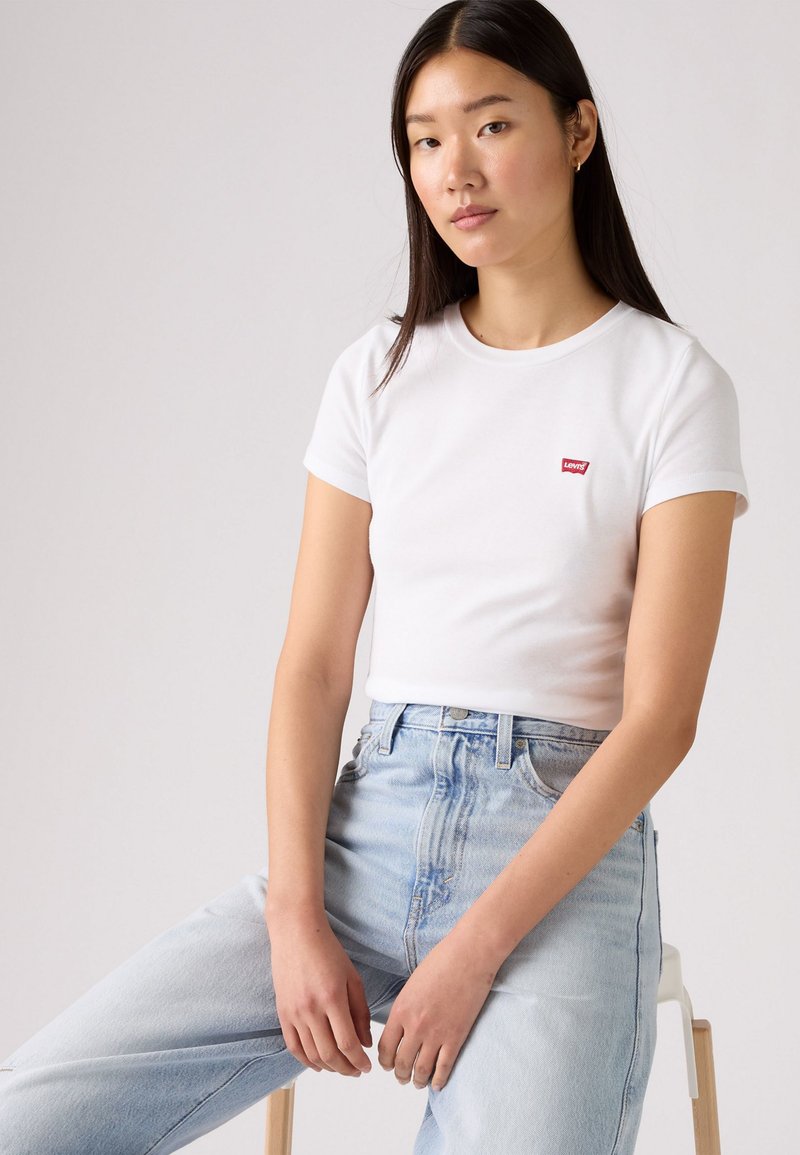 Biele tričko s krátkymi rukávmi a okrúhlym výstrihom, na hrudi s malým červeným logom Levi's, v kombinácii s svetlomodrými džínami so zvýšeným pásom.