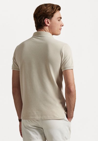 Beige-paita, joka on valmistettu tekstuurikankaasta, lyhythihaisella mallilla ja klassisella kauluksella. Takapuoli on yksinkertainen ja suoralla helman lopetuksella.
