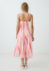 Robe rose jusqu'aux genoux avec fines bretelles, présentant des motifs abstraits fluides dans des nuances de rose et d'orange, fabriquée en tissu léger.