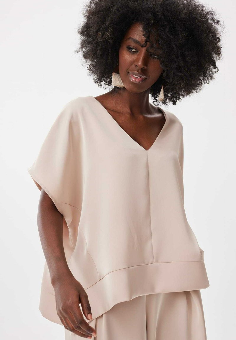 Lichtroze blouse met V-hals, losse mouwen, een rechte snit en een brede zoom. Zachte stof met minimale stikdetails.