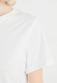 T-shirt en coton blanc avec un col rond, des manches courtes et une texture lisse. Aucune motif ou accent visible.