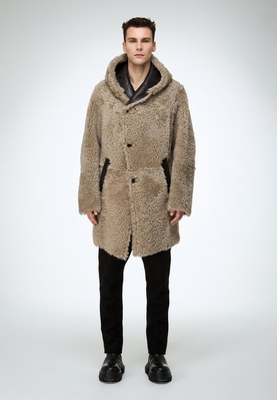 Beżowy płaszcz z sztucznego futra z kapturem, dużymi guzikami z przodu i bocznymi kieszeniami. W połączeniu z czarnymi spodniami i masywnymi czarnymi butami. Gładka faktura.