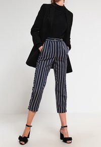 Marinblå och krämfärgade randiga cropped byxor med hög midja och framfickor, kombinerat med en svart kavaj och svarta sandaler med kilklack och remmar.