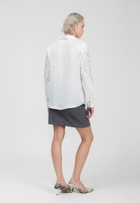 Camicia di seta bianca con maniche decorate, gonna grigia a pois e scarpe con tacco a fantasia. Tessuto morbido, vestibilità su misura e design moderno.