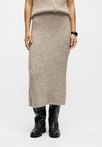 Jupe en mélange de laine tricotée de couleur marron clair avec une forme droite et une taille côtelée. Associée à des bottes en cuir noires.