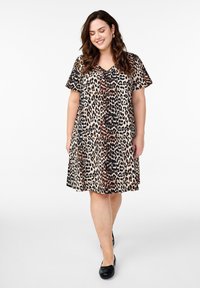 Beżowa sukienka w panterkę z czarnymi i brązowymi plamami. Dekolt w serek, krótkie rękawy, luźny fason, do kolan, zestawiona z czarnymi balerinkami.