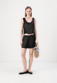 Svart satin ermeløs topp med rund hals og matchende svarte shorts, kombinert med svarte leiligheter og en vevd veske.