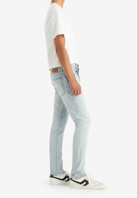 Světlé modré džíny s úzkým střihem, se značením kožené nášivky na zadní straně, jemným odřením a opotřebovanými detaily. Kombinované s bílým tričkem a teniskami.