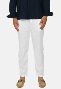 Pantaloni bianchi di lino con taglio dritto, tasche laterali dettagliate e una cintura elastica, abbinati a calzature beige slip-on.