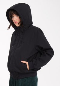 Schwarze Kapuzenjacke aus glattem Stoff, mit einem Reißverschluss vorne, zwei seitlichen Taschen und gerippten Bündchen sowie Saum für eine enge Passform.