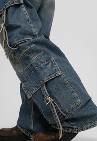 Spodnie cargo z denimu w wyblakłym niebieskim kolorze, z wieloma kieszeniami i luźnym krojem. Zawierają detale przeszyć oraz pasek z srebrną klamrą.