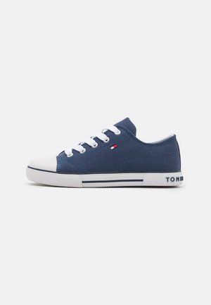 Marineblauwe low-top sneaker met witte veters, witte rubberen neuskap en witte zool met zwarte strepen en een klein logo aan de zijkant.