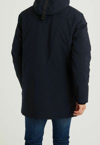 Granatowa kurtka parka z kapturem i regulowanym paskiem, charakteryzująca się gładką fakturą, dłuższym krojem i kieszeniami po bokach. Odpowiednia na chłodne warunki pogodowe.
