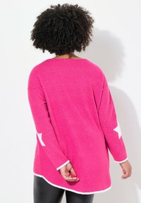 Rosa oversized tröja med vita stjärndetaljer på ärmarna, tillverkad av mjukt, texturerat material. Rundad nederkant och lös passform.