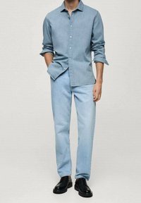 Chemise en denim bleu clair avec col boutonné, associée à un jean droit bleu clair et des chaussures noires à lacets. Coupe décontractée.