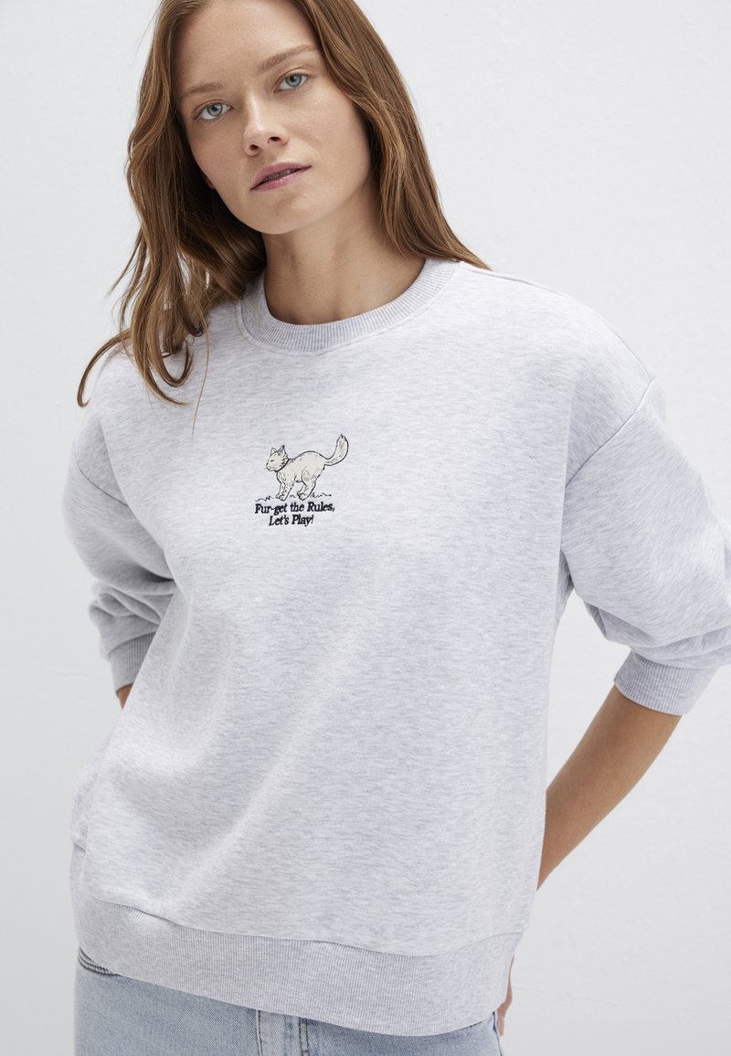 Gray sweatshirt featuring a crew neck, ribbed cuffs, and embroidered cat design with text. Made from soft fabric with a relaxed fit.