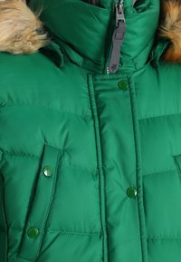 Grön puffjacka med huva fodrad med fuskpäls, dragkedja och tryckknappar, diamantquiltad textur och två framfickor.
