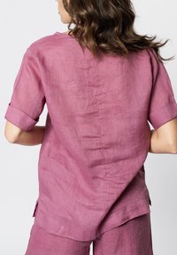 Roze linnen blouse met korte mouwen, voorzien van een ronde halslijn, zijsplitsen en een ontspannen pasvorm, die een subtiele textuur laat zien.