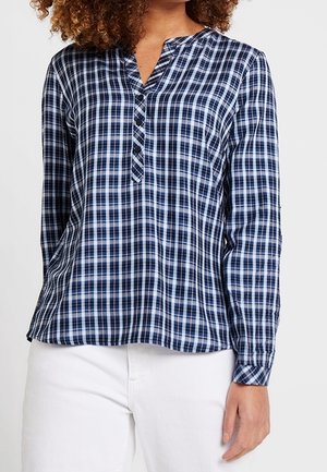 Navyblauw-wit geruit overhemd met lange mouwen en een V-hals met knopen, gedragen met witte broek, zichtbaar van midden torso tot nek.