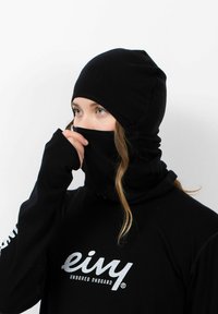 Schwarze Fleece-Mütze mit integriertem Gesichtsschutz, gerippter Textur und erweiterter Nackenabdeckung. Auf der Vorderseite befindet sich ein Logo in Weiß.