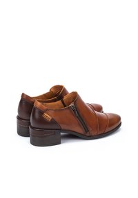 Bottines en cuir marron avec une fermeture éclair sur le côté, un talon empilé, des détails de coutures incurvées et un accent contrastant en brun foncé à l'arrière.