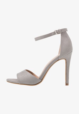 Sandale à talon haut en daim gris clair avec bout ouvert, bride cheville et boucle argentée, vue de profil sur fond blanc.