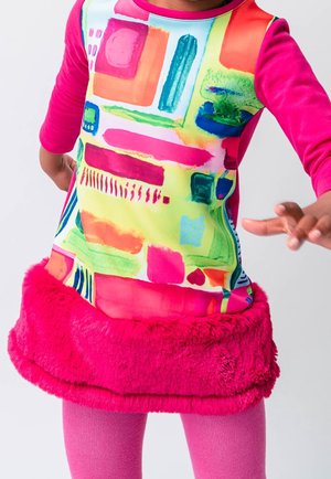 Kolorowa tunika z abstrakcyjnymi wzorami w zieleni, różu i niebieskim, z różowym futrzanym wykończeniem na dole i różowymi leginsami.