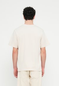Beige cotton t-shirt with short sleeves, crew neck, and relaxed fit. Smooth texture with minimal detailing on the back.