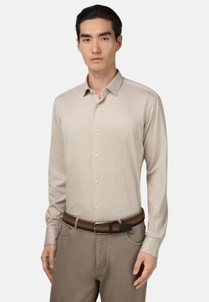 Beige langemouwen overhemd met knopen, gemaakt van zachte stof, met een klassieke kraag en een ontspannen pasvorm. Draagt een gevlochten bruine riem en kaki broek.