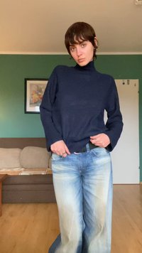 Navy turtleneck sweater with ribbed texture, paired with light blue wide-leg jeans featuring a faded wash. Background includes a brown sofa.