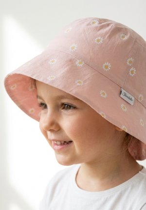 Young child wearing a pink bucket hat with white daisy patterns, smiling and looking slightly to the side against a light background.