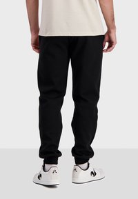 Pantalons de jogging noirs en tissu doux, avec un design fuselé, une taille élastique et des poignets côtelés. Baskets blanches avec des accents noirs.