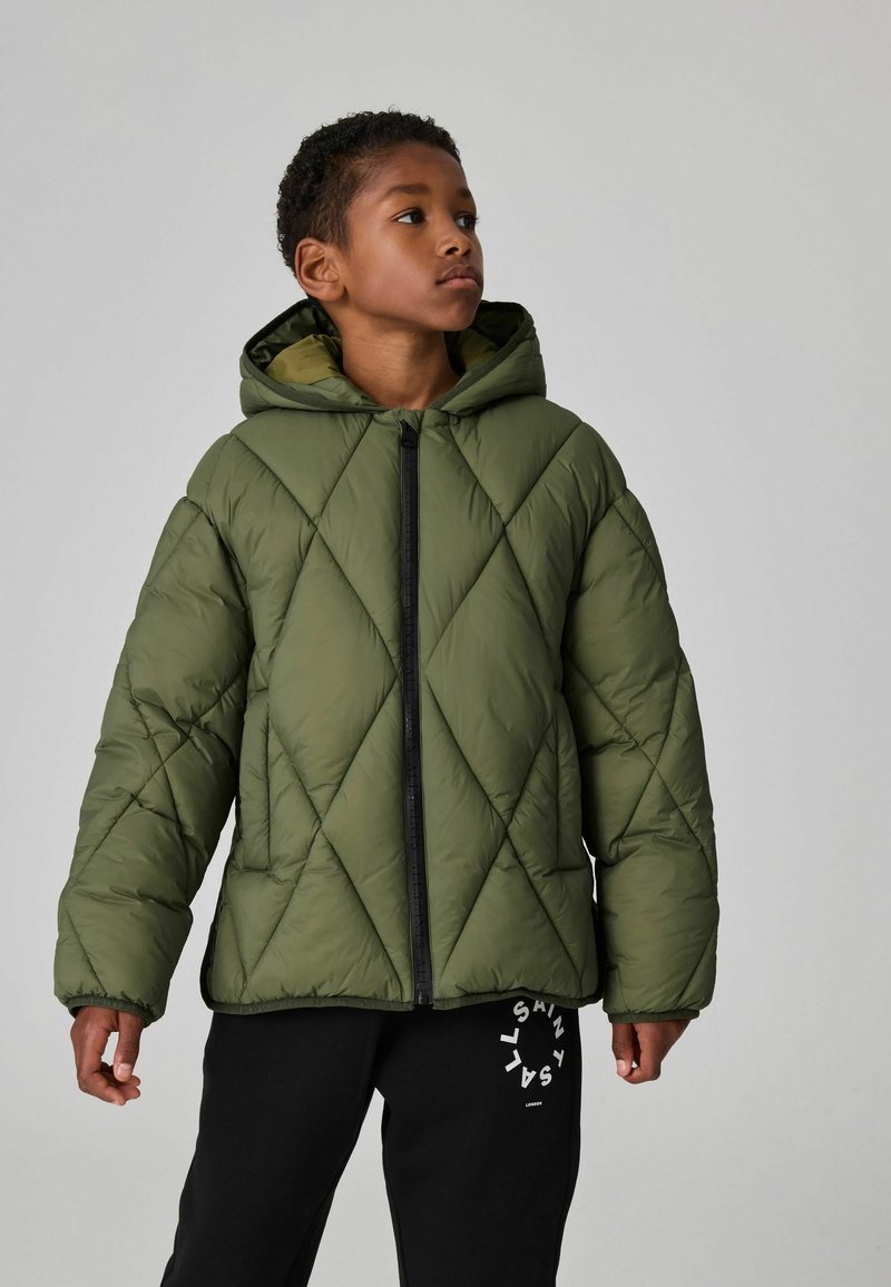 Grön quiltad puffjacka med huva, med en svart dragkedja och diagonala sömmar. Matchad med svarta sweatpants som visar en logotyp.